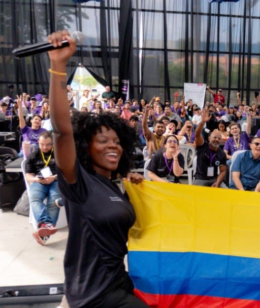 Grace Torres, co-founder, holding a microphone and a Colombian flag in front of an event audience