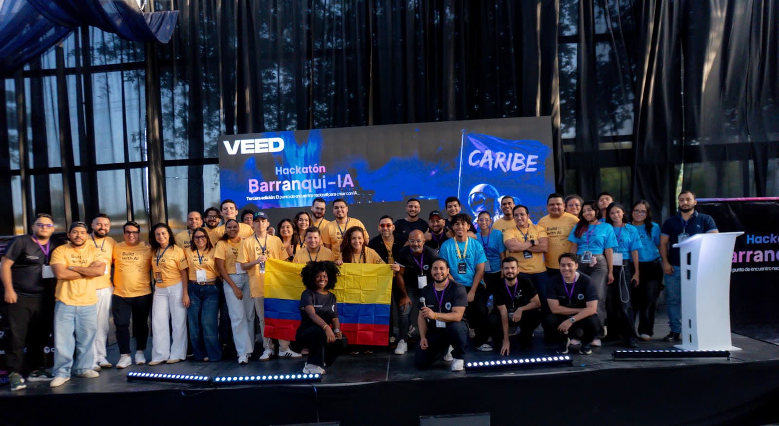 Equipo y participantes de la Hackatón Barranqui-IA posando sobre el escenario con la bandera de Colombia